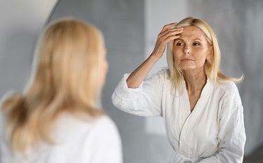 Kobieta w średnim wieku z lwią zmarszczką na czole przegląda się w lustrze